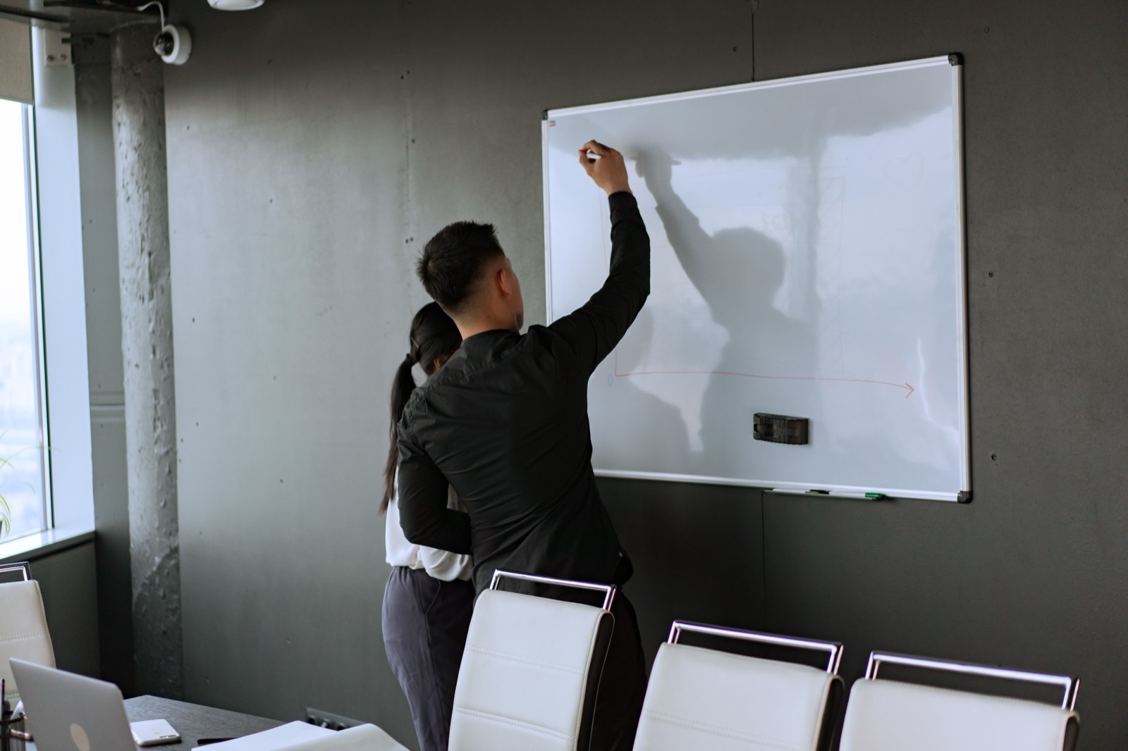 Two people working through a problem at an office whiteboard